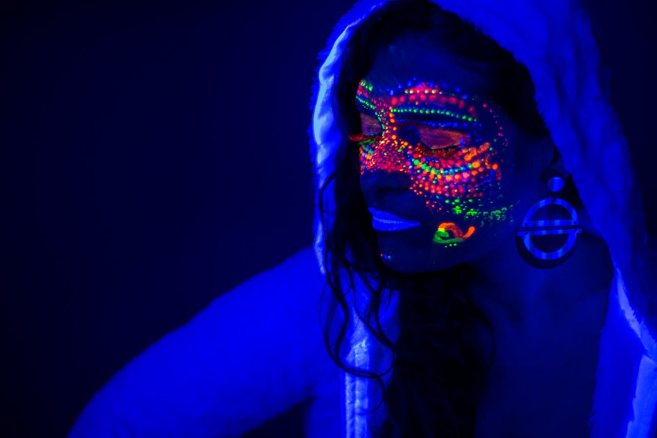 about-us Portrait of a woman with glowing neon paint under UV light creating a futuristic effect.